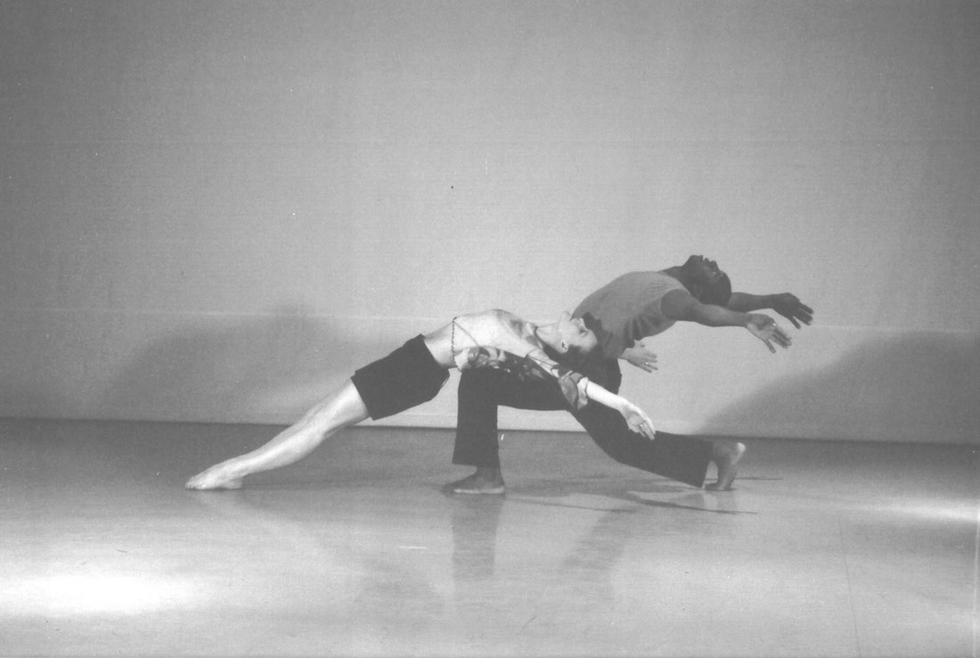 Two dancers leaping in unison, shadows thrown across the wall behind them
