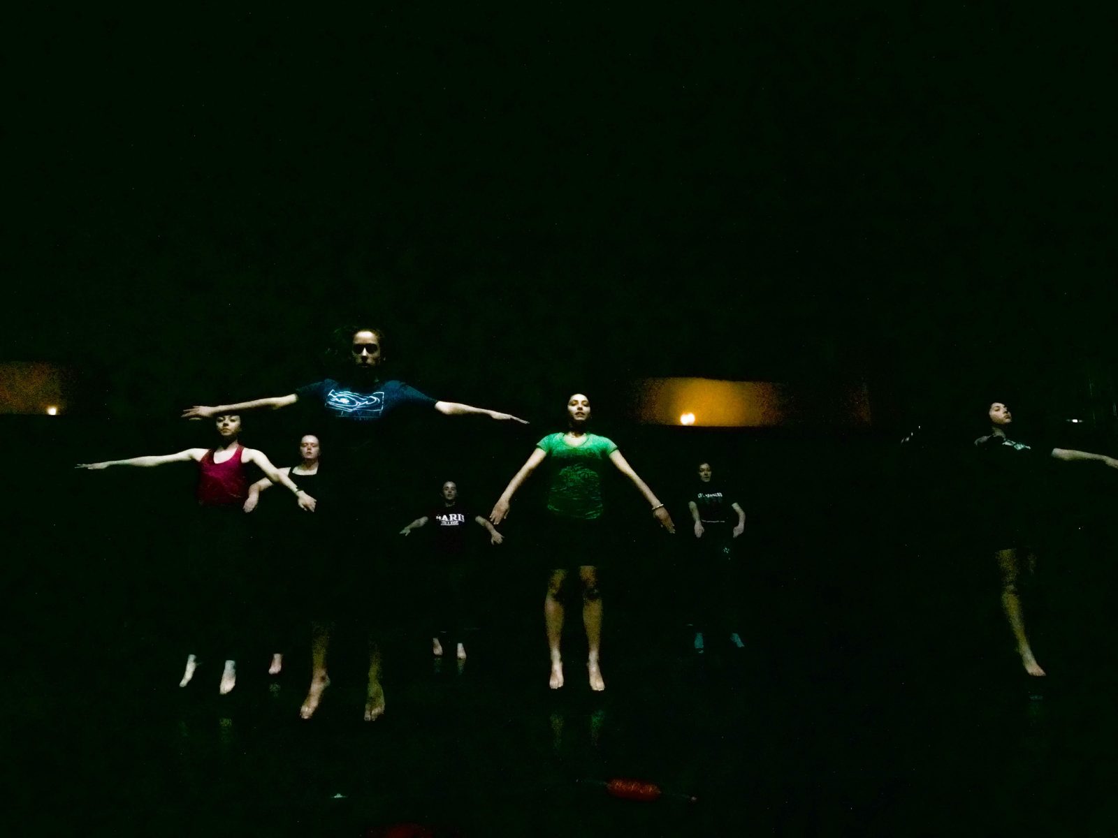 Dancers with arms stretched wide, emerging from darkness in a low light wash