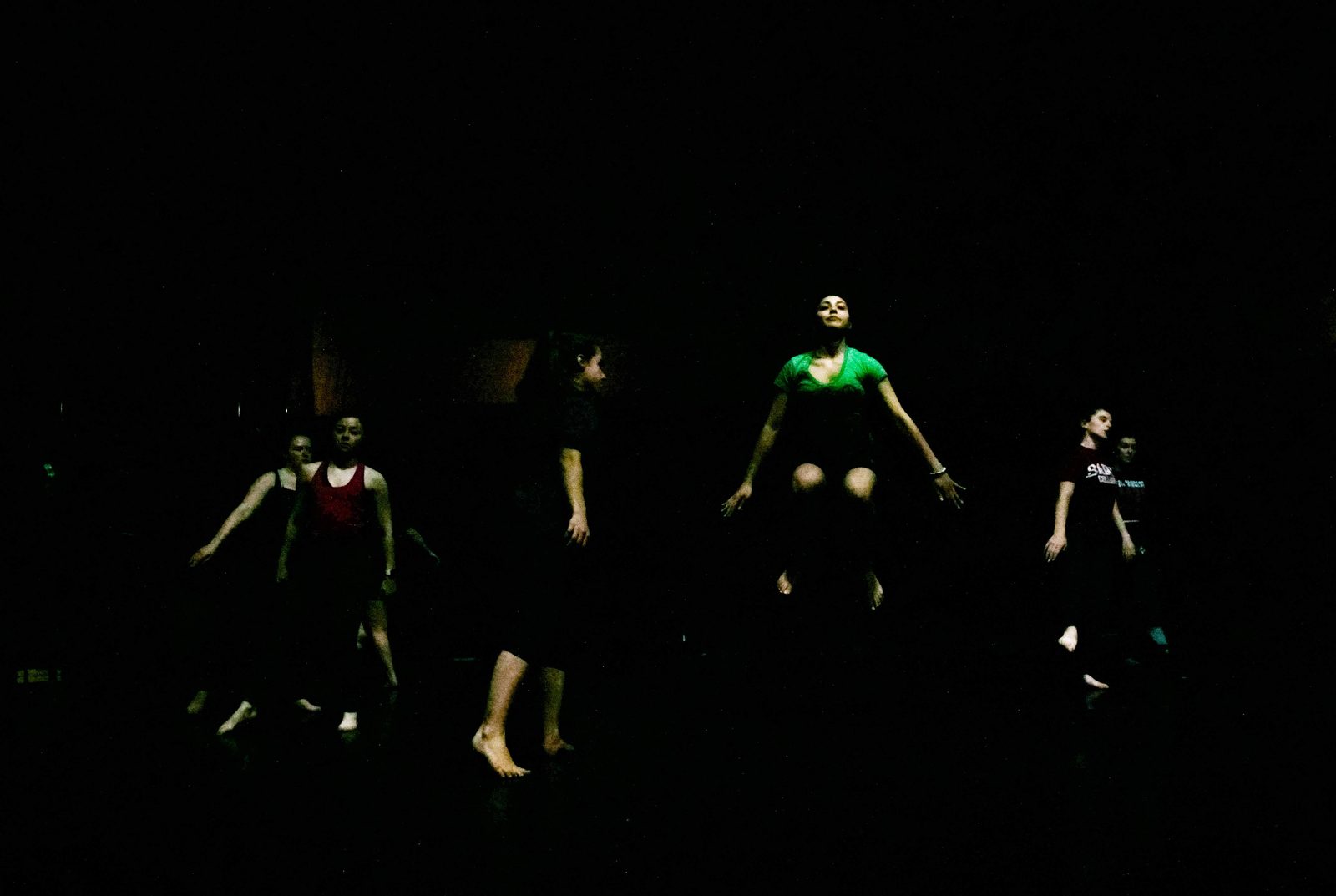 Dancers spaced across a nearly black stage, edges of bodies catching dim light