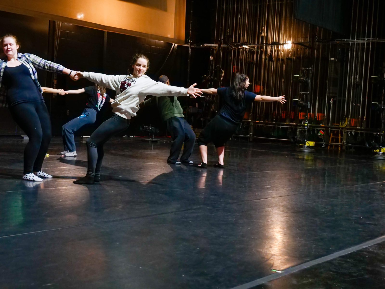 Dancers in a connected chain, arms outstretched, leaning into one another across the stage