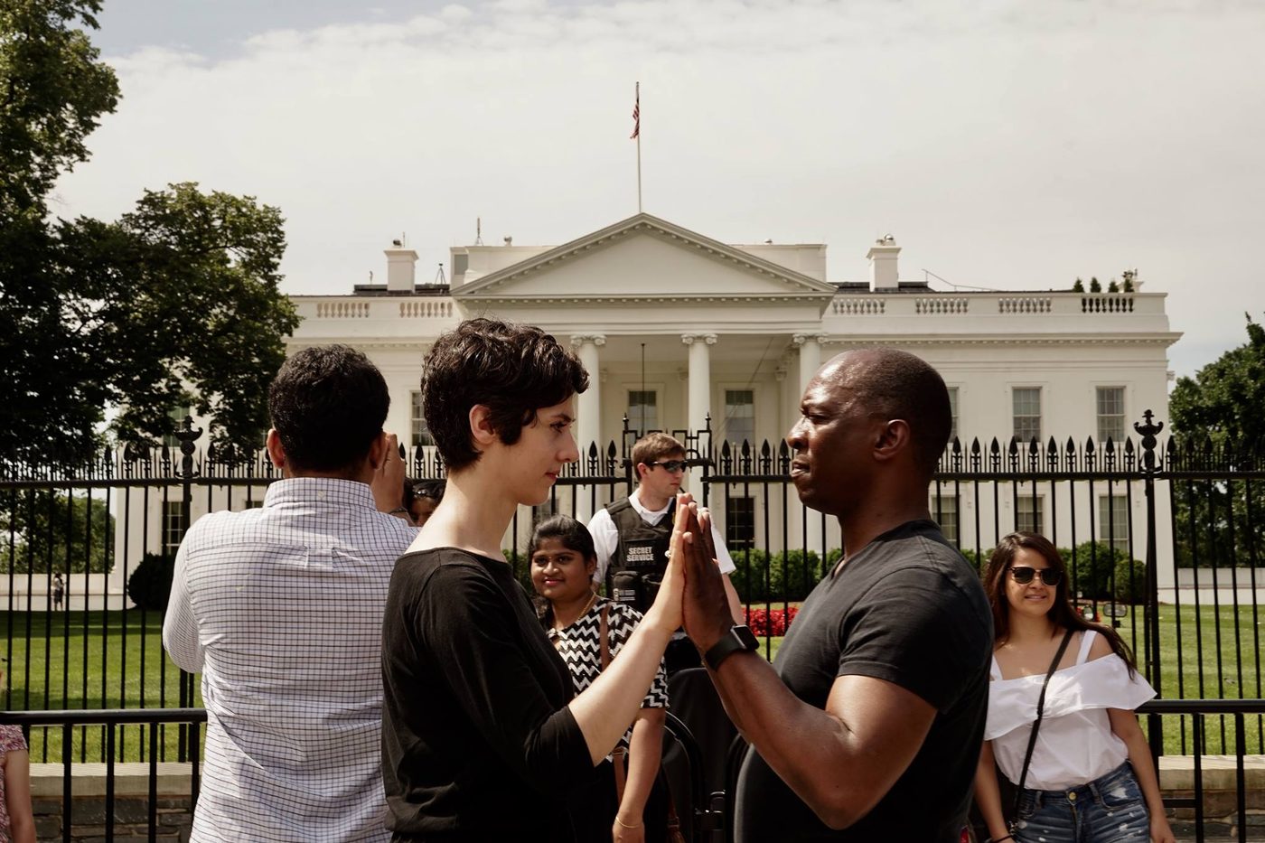 Two people pressing palms together in front of the White House